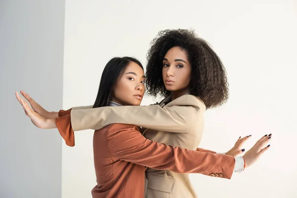 Asian and african american women leaning on wall and looking at camera on white — Stock Photo