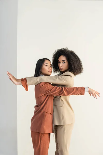 Asian and african american models leaning on wall and looking at camera on white — Stock Photo