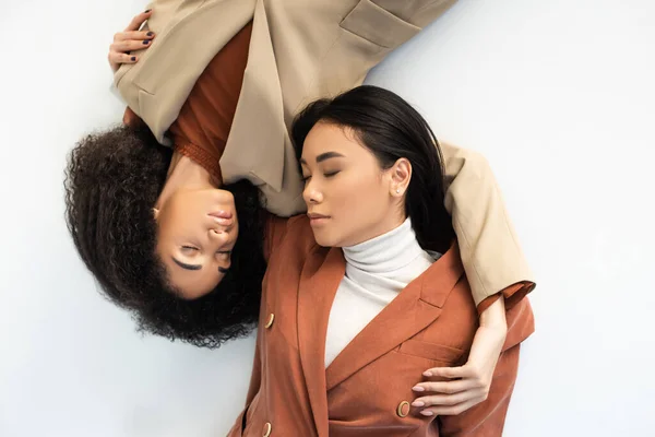 Vista superior de las mujeres americanas asiáticas y africanas en trajes elegantes acostados en blanco - foto de stock