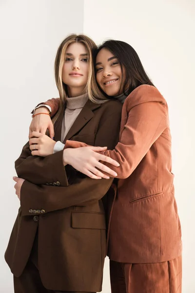 Young stylish model hugging with happy asian friend on white — Stock Photo