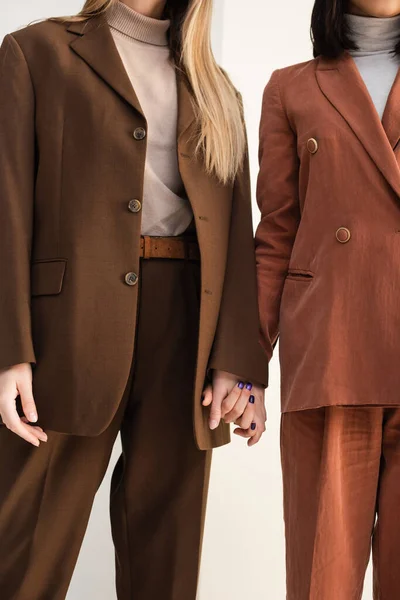 Cropped view of stylish models in suits posing while holding hands on white — Stock Photo