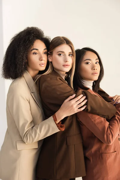 Stylish interracial models in suits hugging while posing on white — Stock Photo