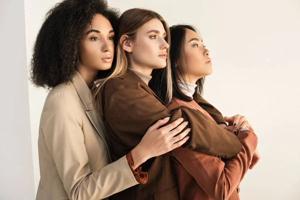 Young and stylish interracial models in suits hugging while posing on white — Stock Photo