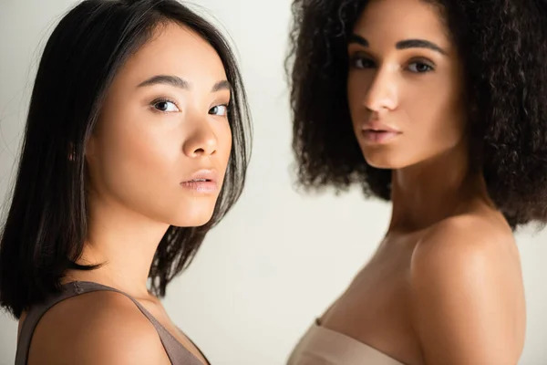 Jóvenes africano americano y asiático las mujeres mirando cámara aislado en blanco - foto de stock
