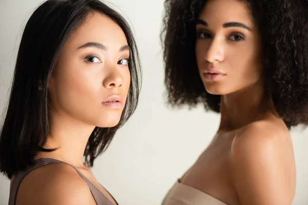 Young african american and asian women looking at camera isolated on white — Stock Photo