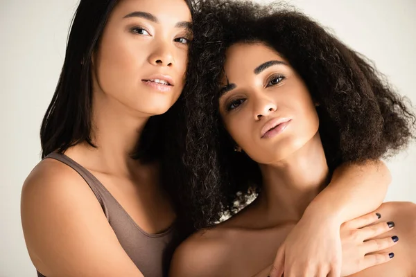 Молодые африканские американские и азиатские женщины обнимаются изолированно на белом — стоковое фото