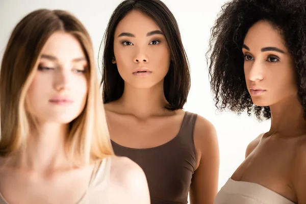 Afro-américaine et asiatique femmes près de blonde modèle sur flou avant-plan isolé sur blanc — Photo de stock