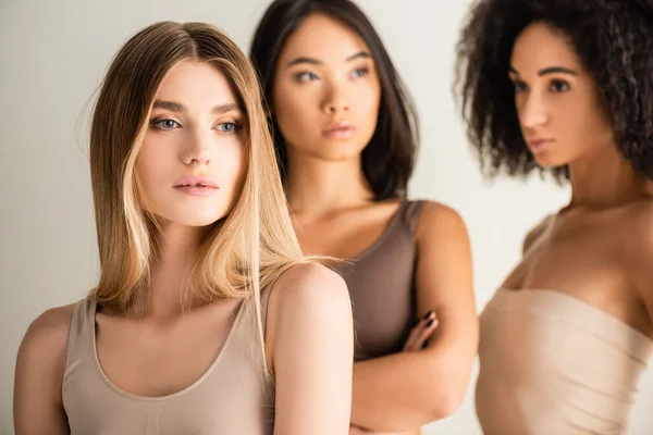 Blondes Modell in der Nähe afrikanischer amerikanischer und asiatischer Frauen auf verschwommenem Hintergrund isoliert auf weißem Hintergrund — Stockfoto