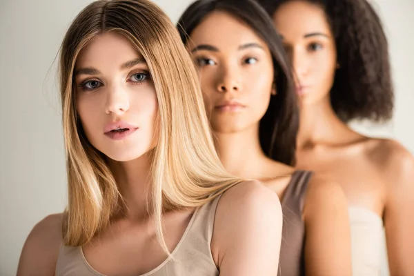 Blonde woman looking at camera near african american and asian models on blurred background isolated on white — Stock Photo
