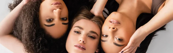 Top view of interracial models looking at camera while lying isolated on white, banner — Stock Photo