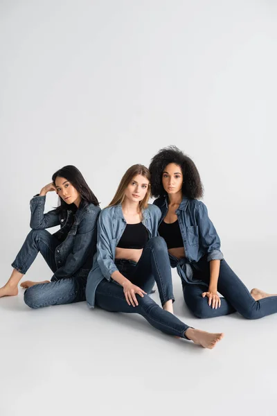 Jóvenes interracial mujeres en denim traje posando en blanco - foto de stock