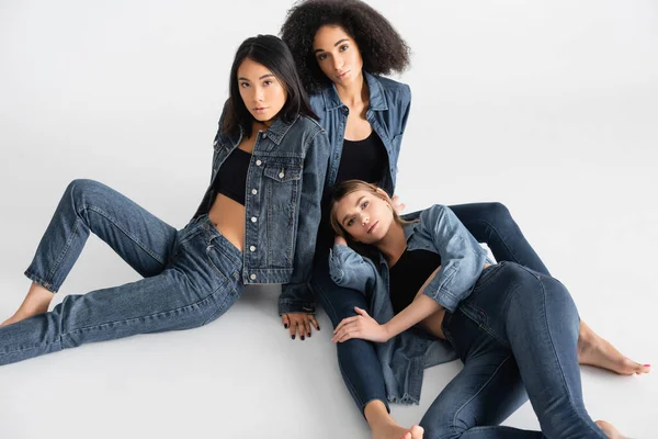 Vue grand angle de jeunes femmes interraciales en tenue denim posant sur blanc — Photo de stock