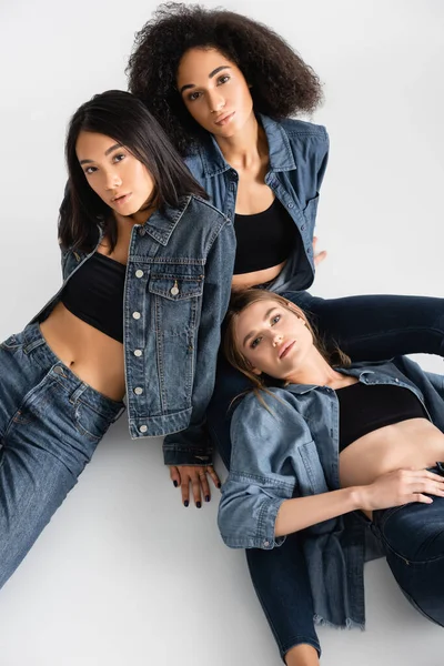 High angle view of trendy interracial women in denim outfit posing on white — Stock Photo