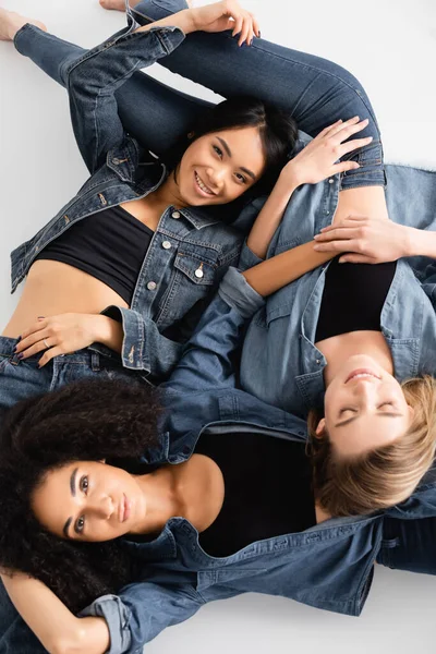 Draufsicht auf junge interrassische Frauen im Jeans-Outfit, die auf Weiß posieren — Stockfoto