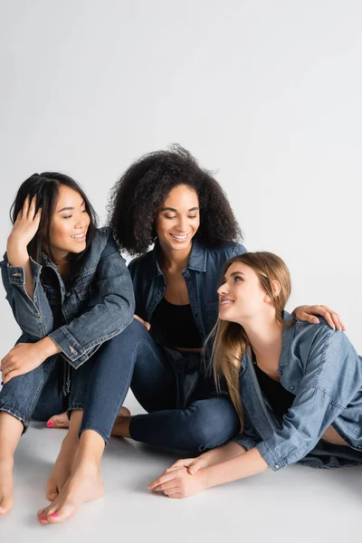 Young interracial women in denim outfit smiling while posing on white — Stock Photo
