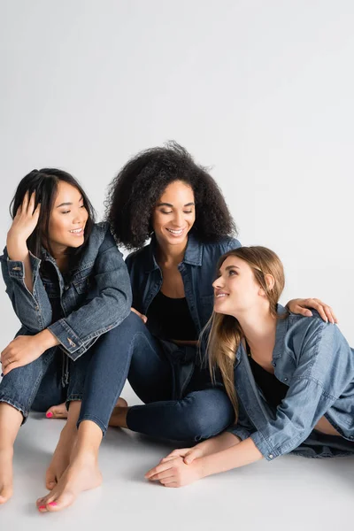 Jóvenes interracial mujeres en denim traje sonriendo mientras posando en blanco - foto de stock