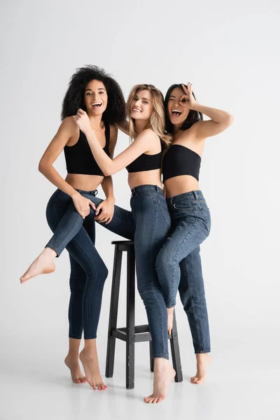 Happy asian woman showing ok sign near interracial models in denim jeans posing on white — Stock Photo