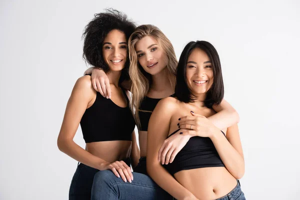 Jóvenes interracial mujeres en tops sonriendo aislado en blanco - foto de stock