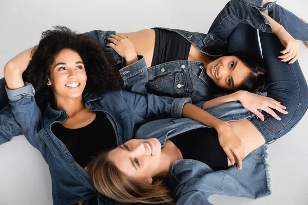 Top view of cheerful young interracial women in denim shirts posing isolated on white — Stock Photo