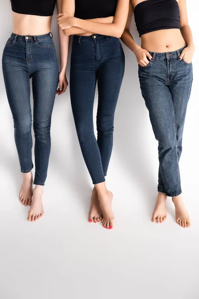 Обрізаний вид молодих жінок в джинсах позує на білому — стокове фото