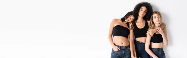 Young interracial women in denim jeans posing on white, banner — Stock Photo