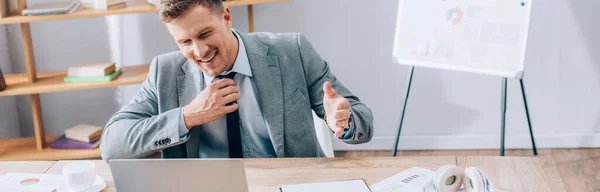 Homme d'affaires souriant ayant chat vidéo sur ordinateur portable près des papiers, tasse et écouteurs sur la table, bannière — Photo de stock