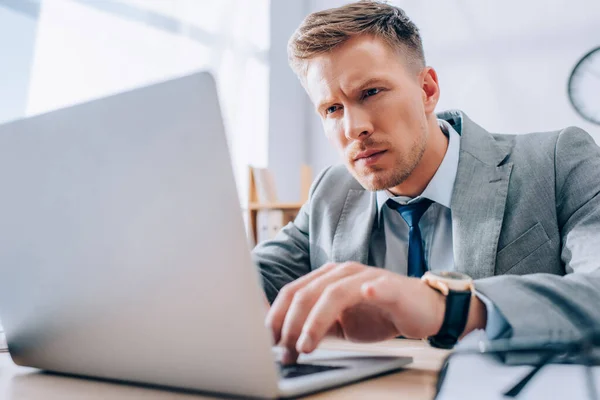 Homme d'affaires concentré utilisant un ordinateur portable au premier plan flou dans le bureau — Photo de stock