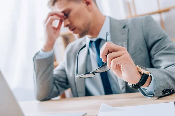 Brille in der Hand eines müden Geschäftsmannes, der Augen auf verschwommenem Hintergrund berührt — Stockfoto