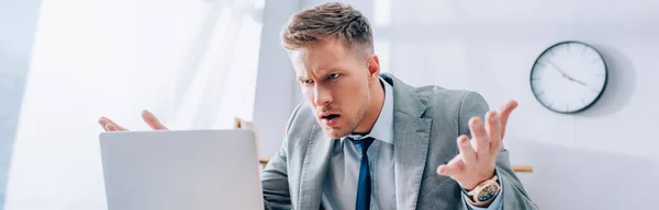 Агрессивный бизнесмен смотрит на ноутбук на размытом переднем плане в офисе, баннер — стоковое фото