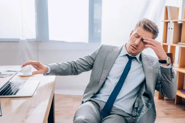 Hombre de negocios cansado tocando el ordenador portátil mientras trabaja en la oficina - foto de stock