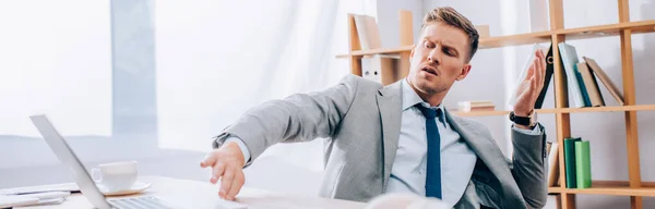 Homme d'affaires confus repoussant ordinateur portable sur le premier plan flou dans le bureau, bannière — Photo de stock