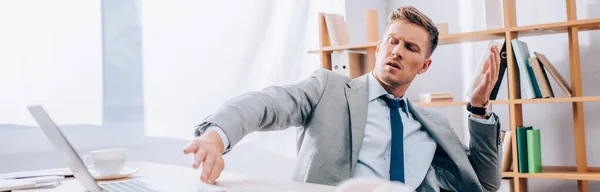 Verwirrter Geschäftsmann schiebt Laptop auf verschwommenem Vordergrund im Büro, Banner — Stockfoto