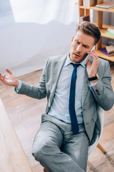 Vista de alto ángulo del hombre de negocios en traje hablando en el teléfono inteligente en la oficina - foto de stock