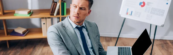 Homme d'affaires tenant ordinateur portable avec écran blanc dans le bureau, bannière — Photo de stock