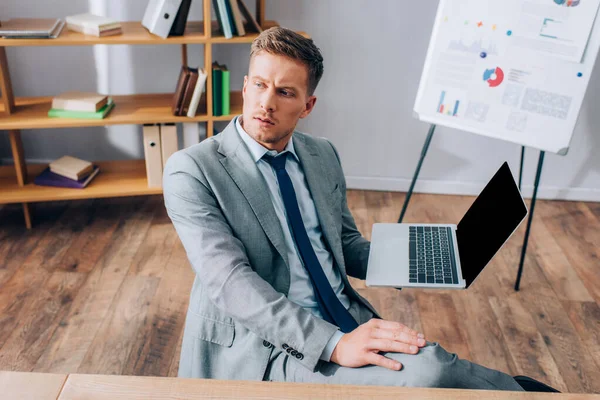 Young businessman in suit holding laptop with blank screen in office — Stock Photo