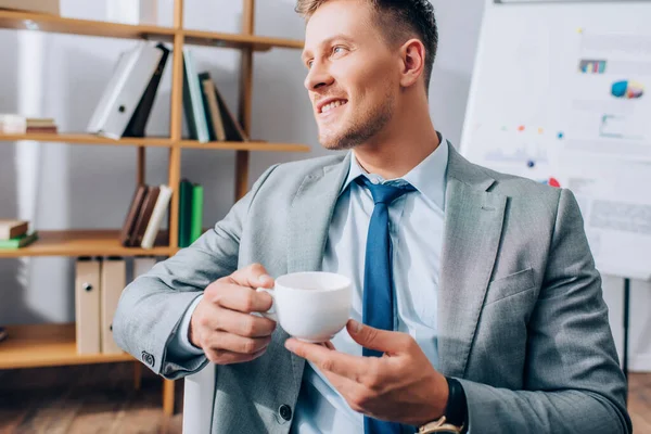 Jovem empresário sorrindo enquanto segura uma xícara de café no escritório — Fotografia de Stock