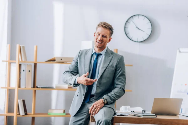 Fröhlicher Geschäftsmann lächelt, während er neben Geräten eine Brille auf dem Arbeitstisch sitzt — Stockfoto