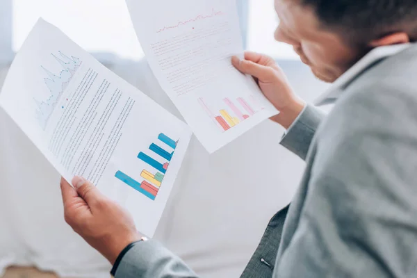 Papers with graphs in hands of businessman talking on smartphone on blurred foreground — Stock Photo