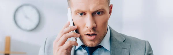 Возбужденный бизнесмен разговаривает на смартфоне в офисе, баннер — стоковое фото