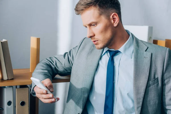 Businessman using smartphone near cupboard with paper folders — Stock Photo