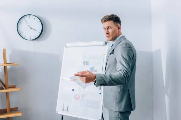 Businessman pointing with finger away near flipchart on blurred background in office — Stock Photo