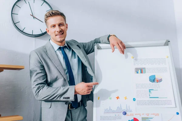 Lächelnder Geschäftsmann zeigt im Büro auf Papiere mit Grafiken auf Flipchart — Stockfoto