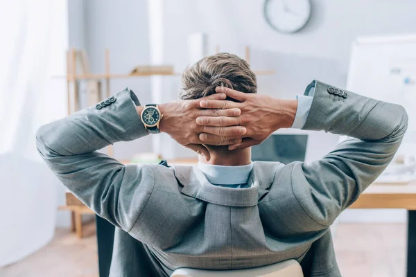 Rückenansicht eines Geschäftsmannes, der während seiner Arbeit im Büro die Hände in Kopfnähe hält — Stockfoto