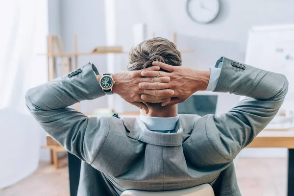 Vista trasera del hombre de negocios cogido de la mano cerca de la cabeza mientras trabaja en la oficina - foto de stock