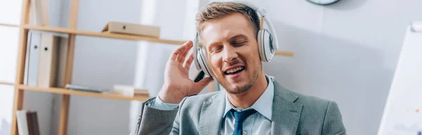 Uomo d'affari positivo che ascolta musica in cuffia in ufficio, banner — Foto stock