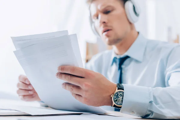 Documents in hands on businessman listening music in headphones on blurred background — Stock Photo