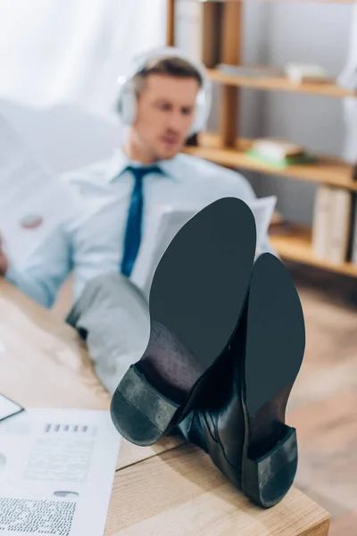 Businessman putting legs on table while working with papers on blurred background — Stock Photo