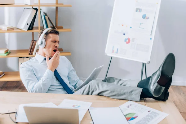 Tired businessman in headphones yawning while doing paperwork in office — Stock Photo