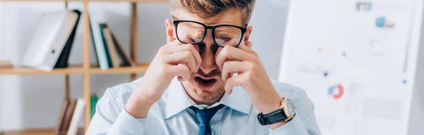 Tired businessman in eyeglasses rubbing eyes in office, banner — Stock Photo