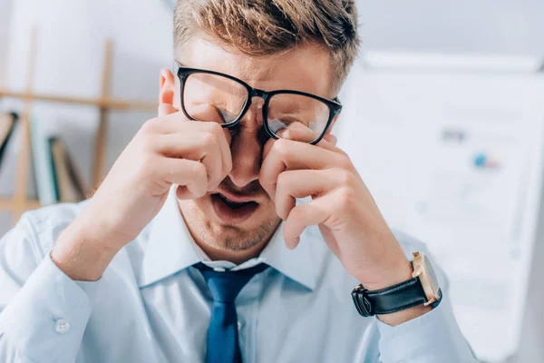 Hombre de negocios agotado frotando los ojos mientras trabaja en la oficina - foto de stock